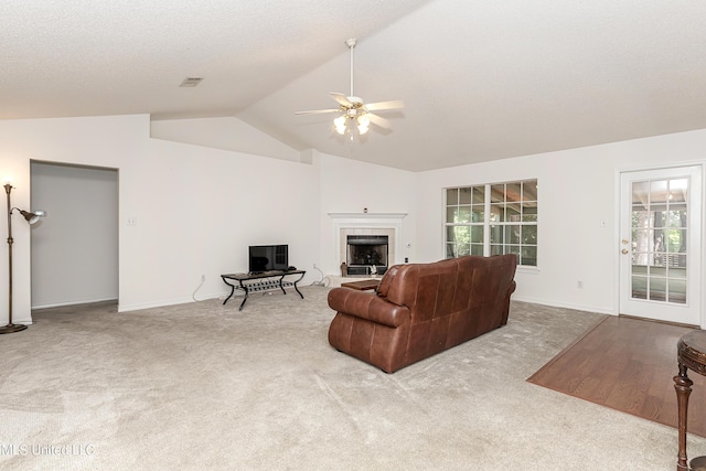 carpeted living room featuring a textured ceiling, vaulted ceiling, ceiling fan, and a tiled fireplace