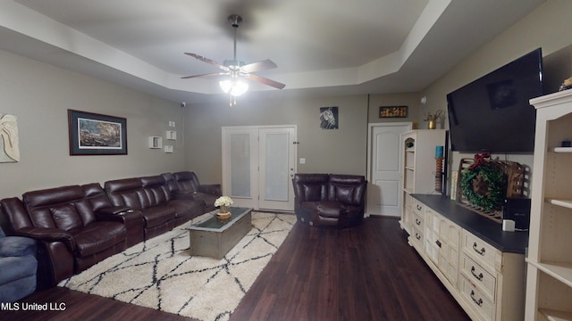 living room featuring ceiling fan, a tray ceiling, and dark hardwood / wood-style floors