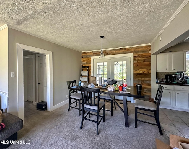 carpeted dining space featuring french doors, a textured ceiling, ornamental molding, and wooden walls