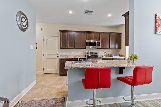 15035 Baylor Ave, Gulfport, MS 39503 - kitchen with appliances with stainless steel finishes, a sink, dark brown cabinets, a kitchen bar, and light stone countertops