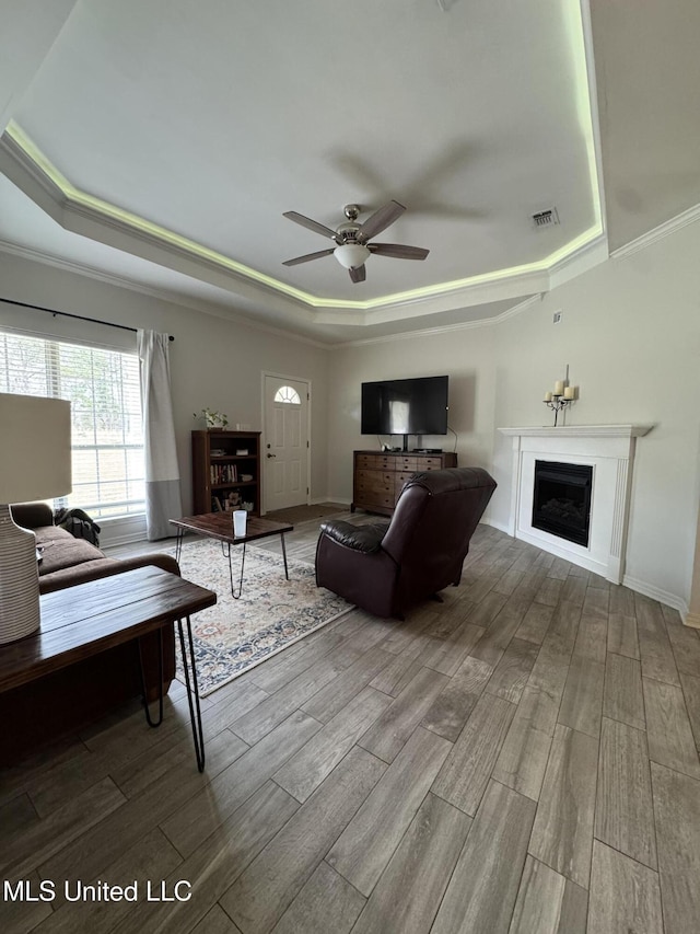 living room with a fireplace, a raised ceiling, visible vents, ceiling fan, and wood finished floors