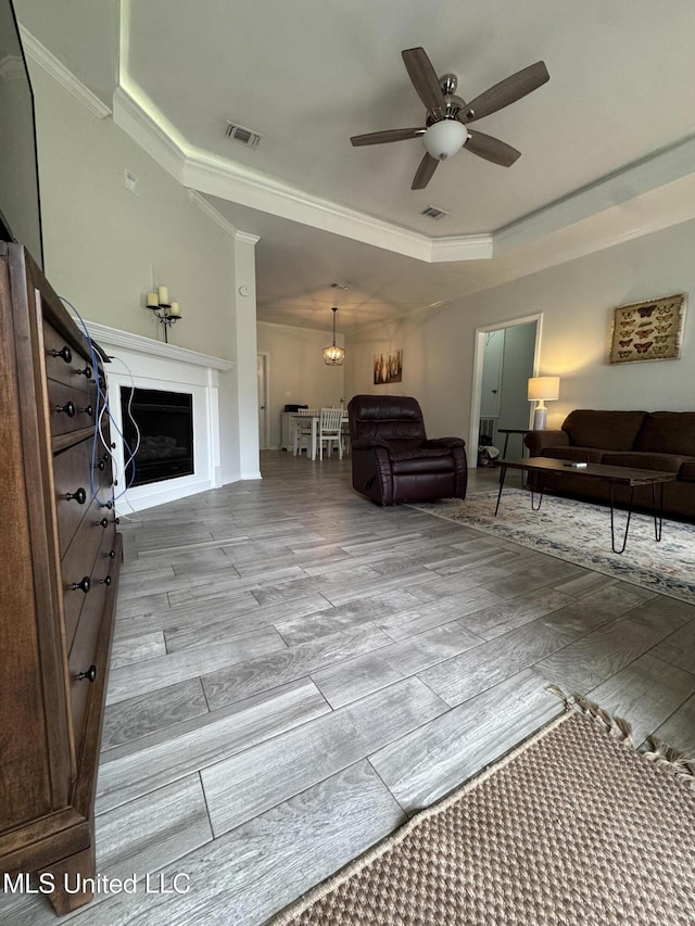 living room featuring a fireplace, visible vents, a raised ceiling, and wood finished floors