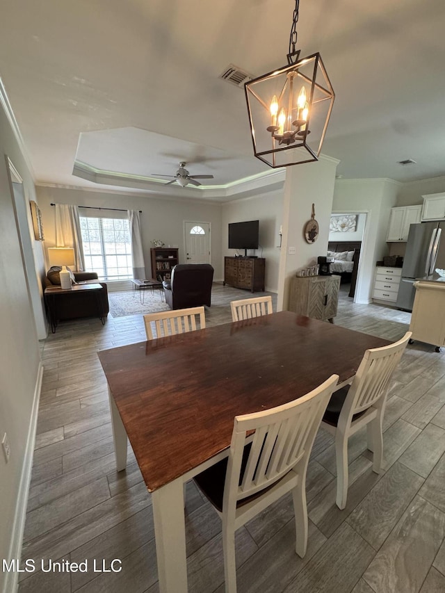 dining room featuring wood tiled floor, visible vents, ornamental molding, and a raised ceiling