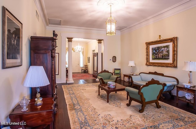 sitting room featuring a notable chandelier, dark wood-type flooring, ornamental molding, and ornate columns