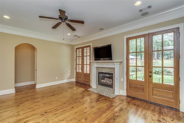 unfurnished living room featuring light wood-type flooring, arched walkways, french doors, and crown molding