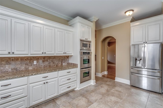 kitchen with arched walkways, light stone counters, appliances with stainless steel finishes, ornamental molding, and tasteful backsplash