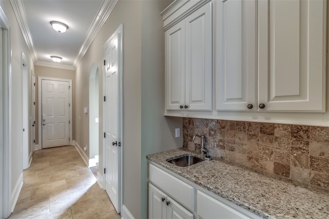 interior space with arched walkways, crown molding, decorative backsplash, a sink, and baseboards