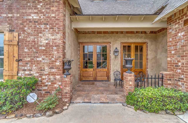 property entrance featuring french doors, brick siding, and roof with shingles