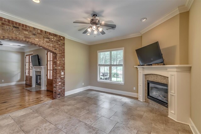 unfurnished living room with ceiling fan, ornamental molding, baseboards, and a glass covered fireplace