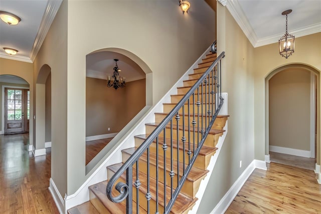 stairway featuring a chandelier, arched walkways, crown molding, and wood finished floors