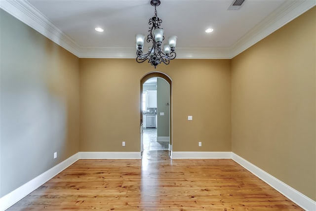 spare room featuring arched walkways, visible vents, light wood-style floors, baseboards, and crown molding