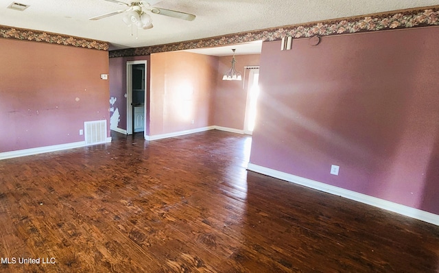 empty room with ceiling fan with notable chandelier, dark hardwood / wood-style flooring, and a textured ceiling