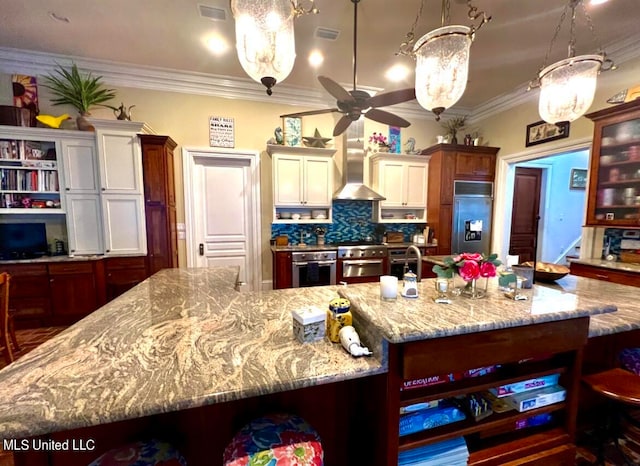 kitchen featuring a large island, wall chimney exhaust hood, paneled built in fridge, decorative light fixtures, and stainless steel oven