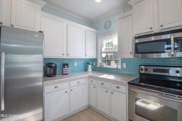 kitchen featuring backsplash, stainless steel appliances, white cabinets, crown molding, and tile counters