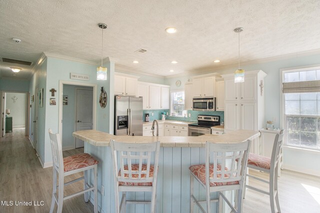 kitchen with tasteful backsplash, ornamental molding, appliances with stainless steel finishes, light wood-style floors, and a sink