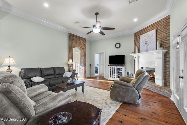 living room with ornamental molding, a warm lit fireplace, and wood-type flooring