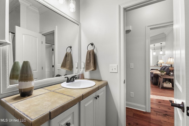 bathroom featuring baseboards, wood finished floors, vanity, and crown molding