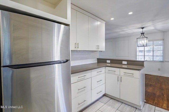 kitchen with kitchen peninsula, decorative light fixtures, white cabinetry, decorative backsplash, and stainless steel refrigerator