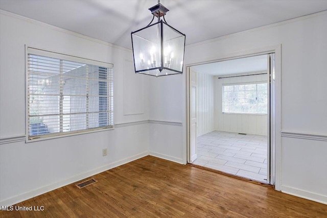 unfurnished dining area featuring hardwood / wood-style flooring, an inviting chandelier, and ornamental molding