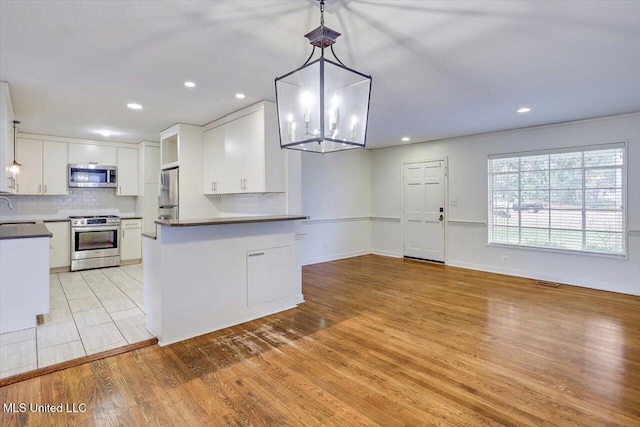 kitchen with white cabinets, pendant lighting, decorative backsplash, and appliances with stainless steel finishes