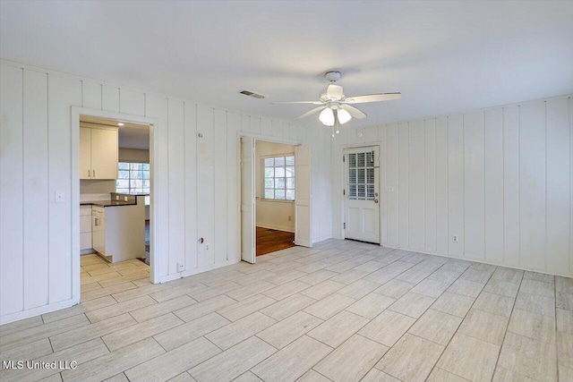 unfurnished room featuring ceiling fan, wood walls, and plenty of natural light