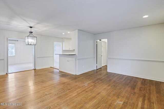 unfurnished living room with light wood-type flooring and a notable chandelier