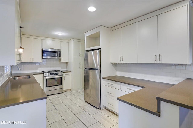 kitchen featuring pendant lighting, white cabinets, stainless steel appliances, sink, and backsplash