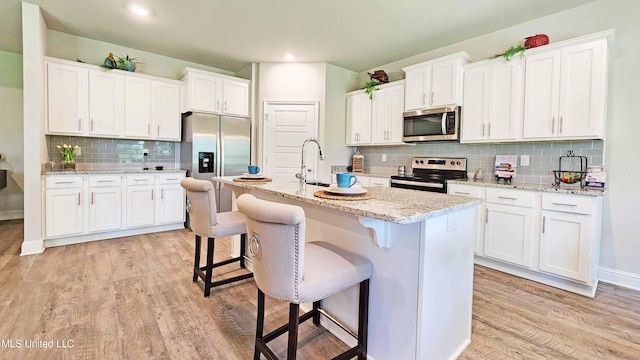15109 Windmill Ridge Parkway, Diberville, MS 39540 - kitchen with appliances with stainless steel finishes, decorative backsplash, white cabinets, light wood-type flooring, and a kitchen bar
