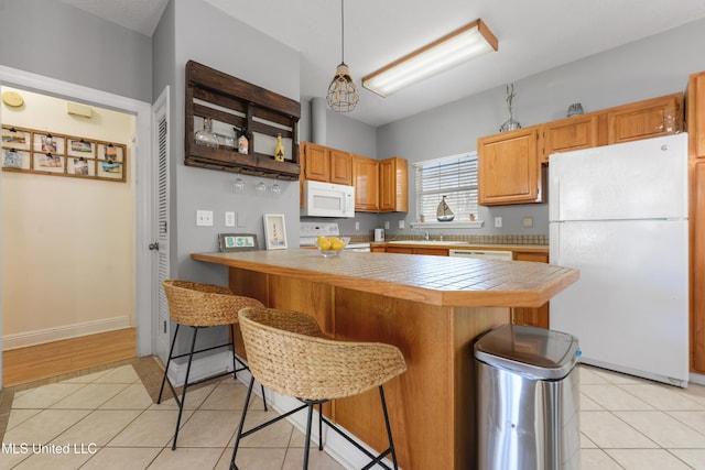 kitchen featuring a breakfast bar area, tile counters, light tile patterned flooring, white appliances, and a peninsula