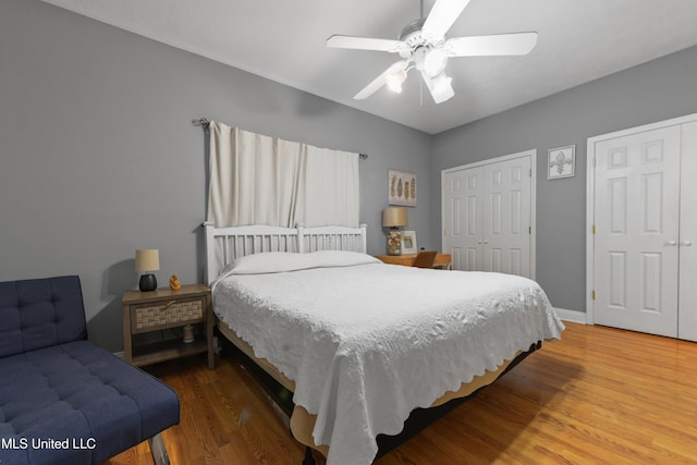 bedroom with a ceiling fan, wood finished floors, two closets, and baseboards