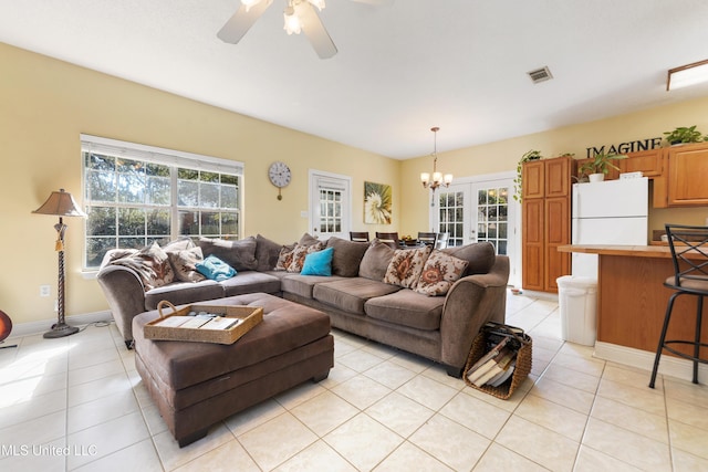 living area with ceiling fan with notable chandelier, french doors, a healthy amount of sunlight, and light tile patterned floors