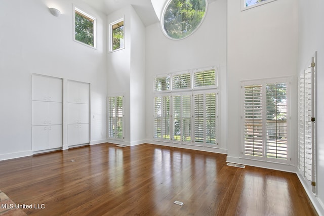 unfurnished living room with a towering ceiling, a healthy amount of sunlight, and dark hardwood / wood-style flooring