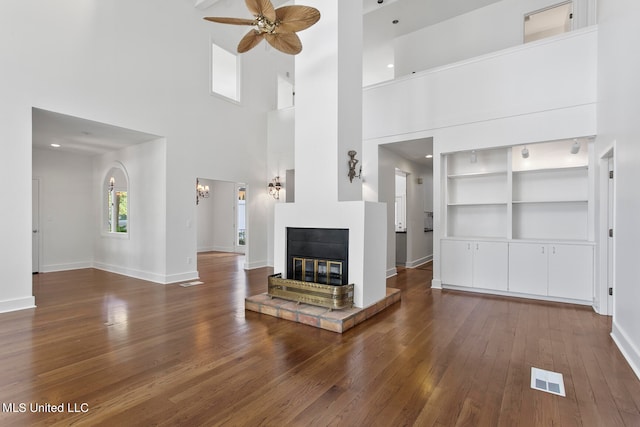 unfurnished living room with ceiling fan, a towering ceiling, dark hardwood / wood-style flooring, and built in shelves