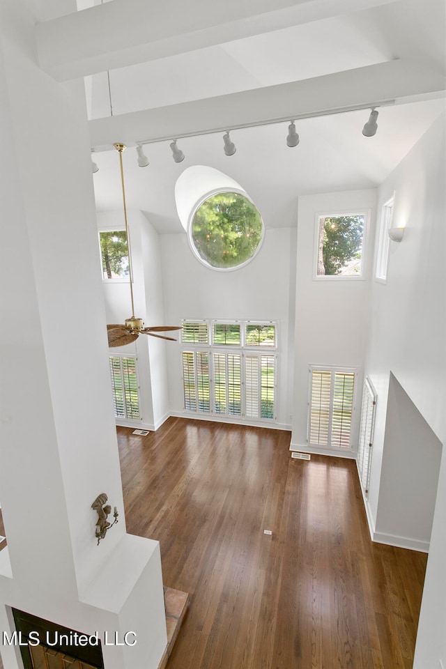 living room with rail lighting, a towering ceiling, beam ceiling, and dark hardwood / wood-style floors