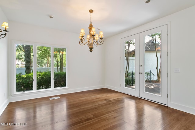 unfurnished dining area with dark wood-type flooring, a notable chandelier, french doors, and plenty of natural light