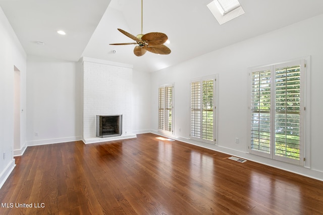 unfurnished living room featuring dark wood-type flooring, ceiling fan, lofted ceiling with skylight, and a fireplace