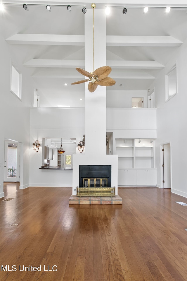 unfurnished living room with a towering ceiling, hardwood / wood-style flooring, and beamed ceiling