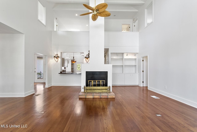 unfurnished living room with ceiling fan, a towering ceiling, beam ceiling, and hardwood / wood-style floors