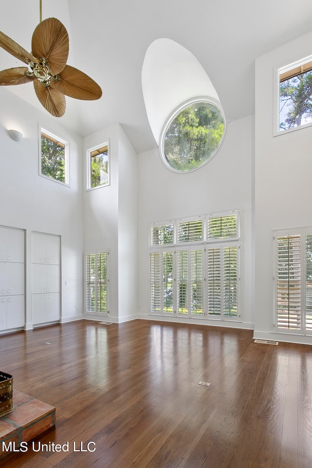 unfurnished living room featuring ceiling fan, wood-type flooring, a high ceiling, and a wealth of natural light