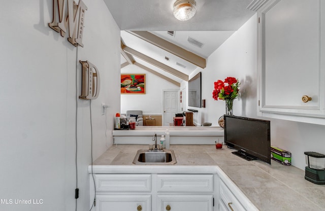 interior space with lofted ceiling with beams, white cabinetry, tile counters, and sink