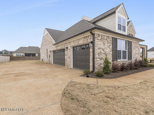 view of property exterior with driveway, a garage, fence, and brick siding