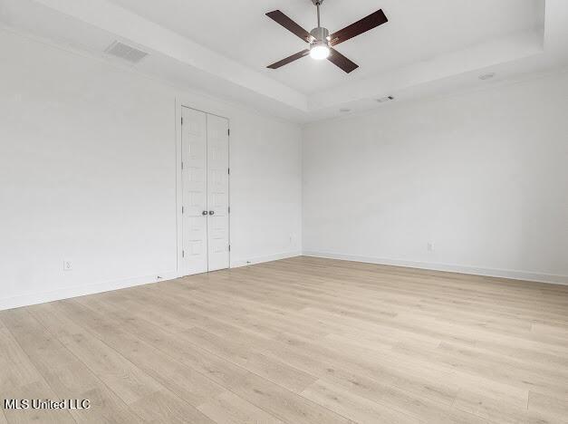 unfurnished room with ceiling fan, a tray ceiling, and light hardwood / wood-style flooring