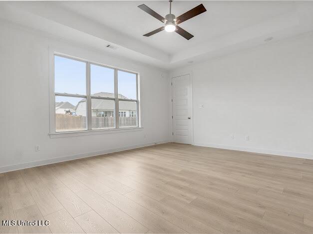 unfurnished room with light hardwood / wood-style flooring, ceiling fan, and a tray ceiling