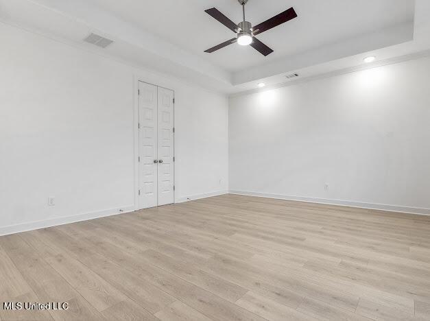 spare room with a raised ceiling, ceiling fan, and light hardwood / wood-style flooring