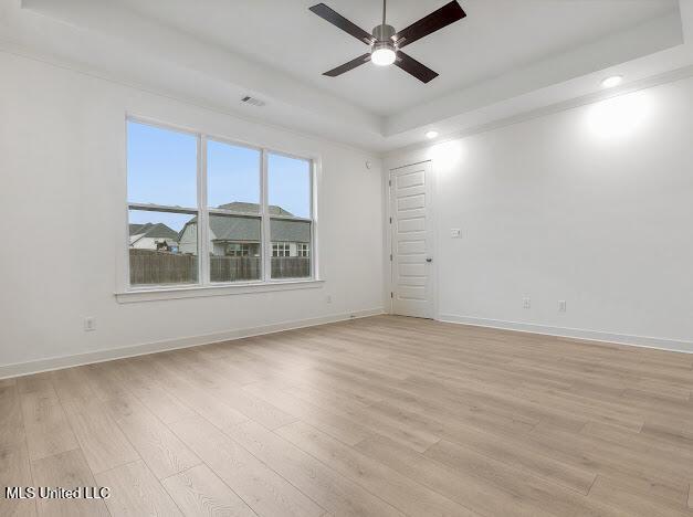 empty room with a tray ceiling, ceiling fan, and light wood-type flooring