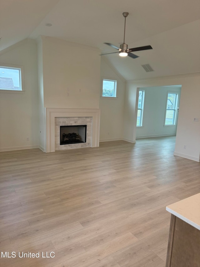 unfurnished living room with lofted ceiling, a tile fireplace, ceiling fan, and light wood-type flooring