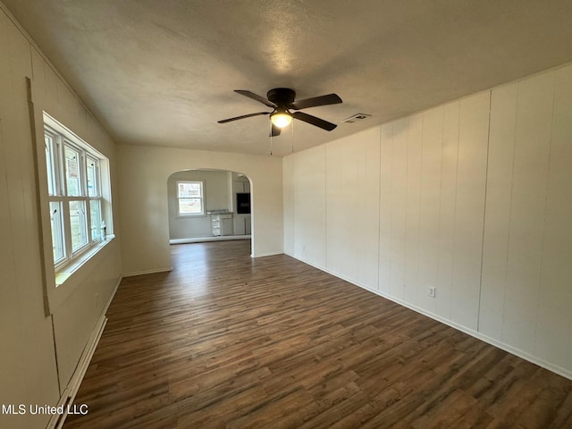 unfurnished living room featuring visible vents, a ceiling fan, a textured ceiling, dark wood finished floors, and arched walkways