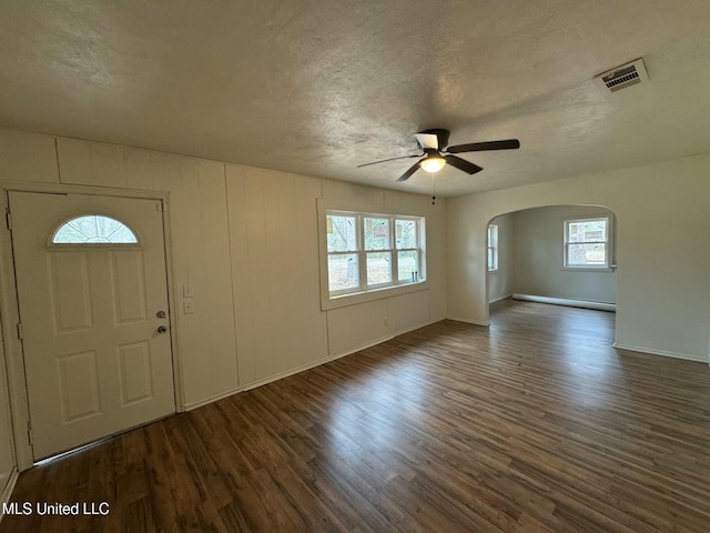 foyer entrance with visible vents, wood finished floors, arched walkways, a textured ceiling, and a ceiling fan