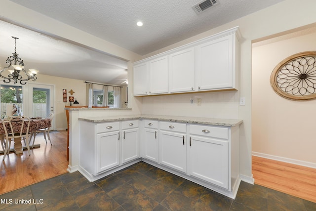 kitchen with a textured ceiling, kitchen peninsula, white cabinets, and dark hardwood / wood-style floors