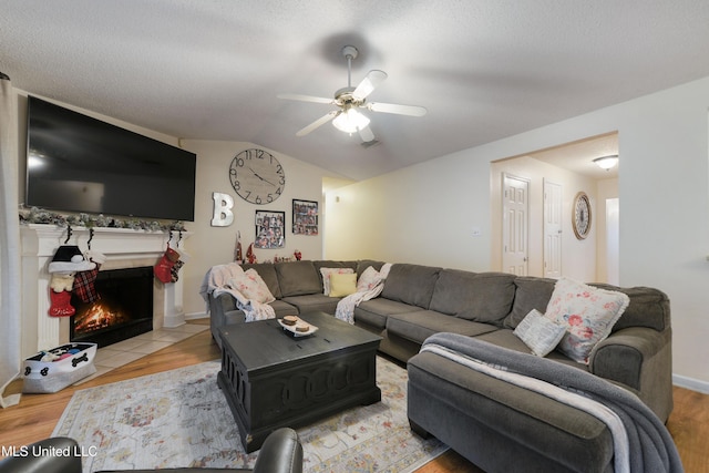 living room featuring a textured ceiling, ceiling fan, vaulted ceiling, and light wood-type flooring